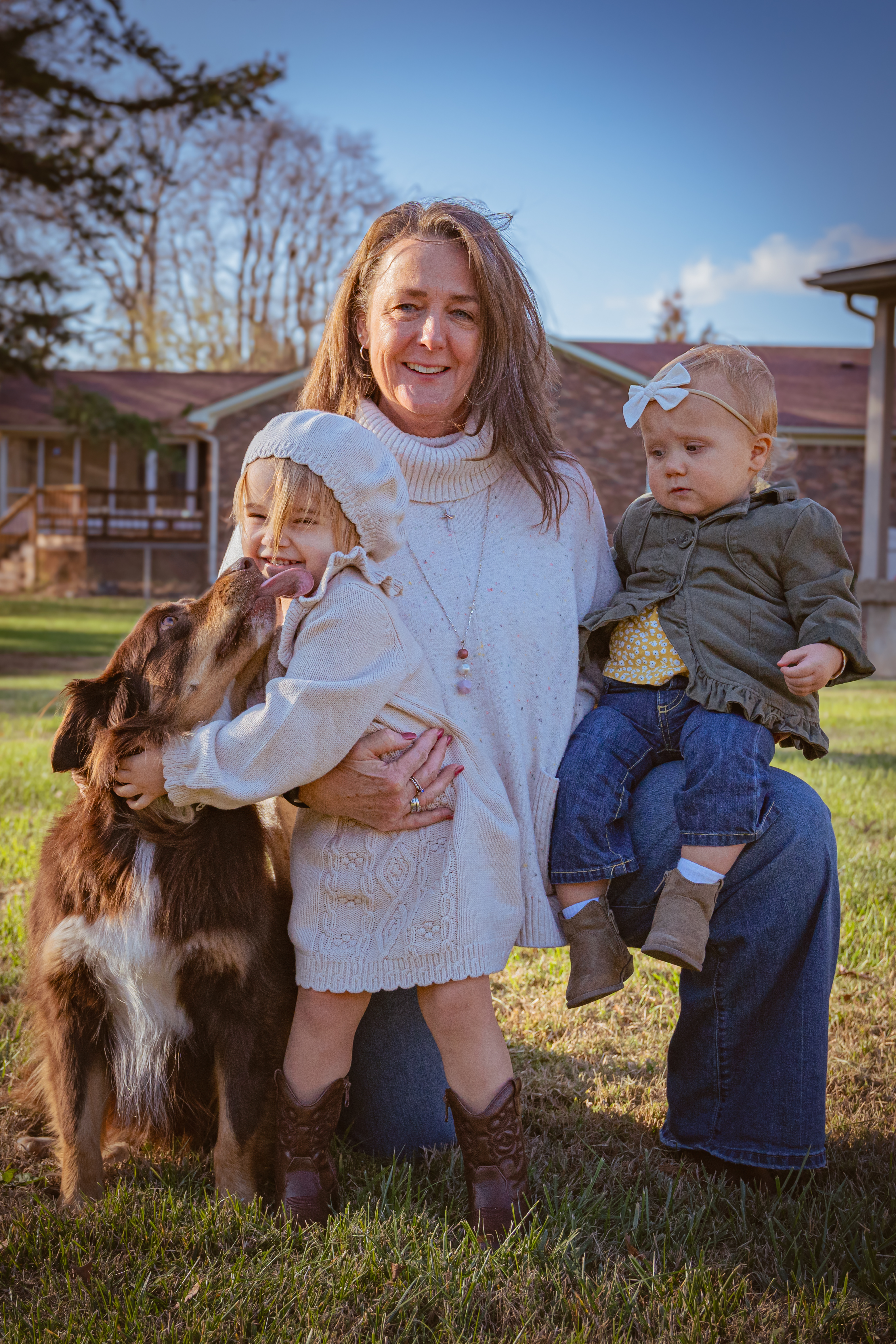 Picture of host with grandchildren and dog on their knee in a grassy yard
